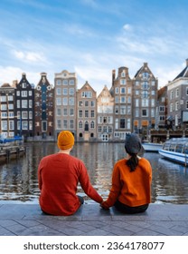  a couple of men and a woman visit the city of Amsterdam with orange colors alongside the canal men and women mid age city trip to Amsterdam