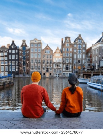  a couple of men and a woman visit the city of Amsterdam with orange colors alongside the canal men and women mid age city trip to Amsterdam
