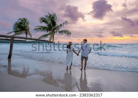 a couple of men and woman watching the sunset on the beach of Koh Kood Island Thailand Trat, a tropical beach with palm trees and a turqouse colored ocean, Ko Kut Island