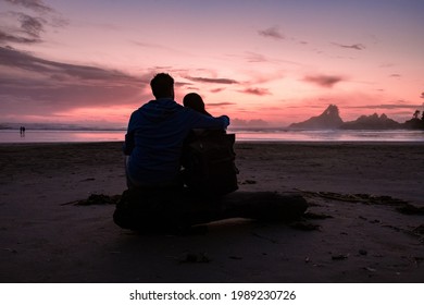 couple of men and women mid-age watching the sunset on the beach of Tofino Vancouver Island Canada, beautiful sunset on the beach with pink-purple colors in the sky. Canada Tofino