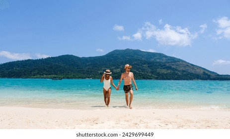 A couple of men and women on the beach of Koh Lipe Island Thailand, a tropical Island with a blue ocean, and white sand. caucasian man in a swim short and an Asian Thai woman in a bikini on the beach - Powered by Shutterstock