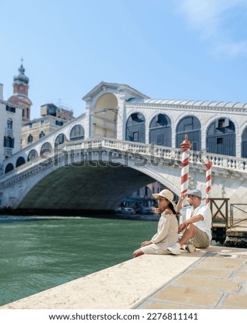 a couple of men and women on a city trip in Venice Italy sitting at the waterfront of the Rialto bridge in Venice, Italy. Architecture and landmark of Venice.cityscape of Venice Italy during summer