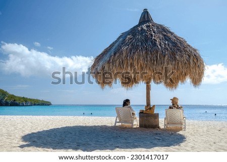A couple of men and women on vacation in Curacao, Cas Abao Beach Playa Cas Abao Caribbean island of Curacao, Playa Cas Abao tropical white beach with beach chairs and a tatched beach umbrella  Imagine de stoc © 