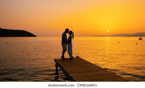 a couple of men and women on a wooden jetty looking at a colorful sunset on the sea, men and women watching a sunset in Crete Greece Europe on a wooden pier in the ocean at dusk - Powered by Shutterstock