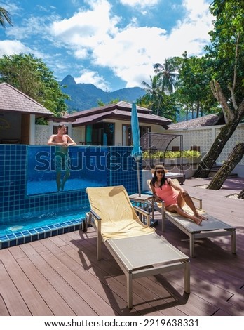 A couple of men and women relaxing by the swimming pool of a luxury pool villa during a vacation. Thao women and caucasian men on a luxury vacation