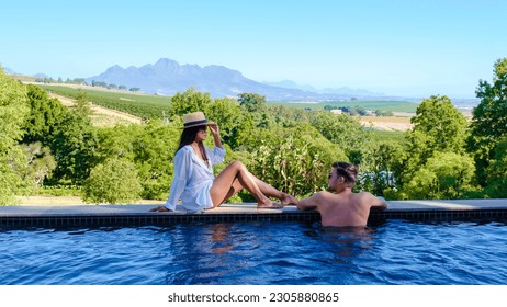 Couple of men and women relaxing at a swimming pool with a view over a Vineyard landscape at sunset with mountains in Stellenbosch, near Cape Town, South Africa.  - Powered by Shutterstock