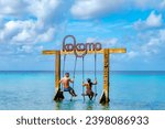 Couple of men and women at a swing in the ocean of Curacao Caribbean Island, Kokomo Beach at the Caribbean island of Curacao on a sunny day