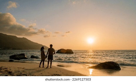 A couple of men and women watching the sunset o a tropical beach at the Seychelles Islands. 