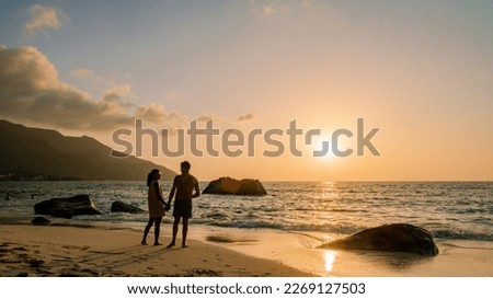 A couple of men and women watching the sunset o a tropical beach at the Seychelles Islands. 
