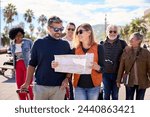 Couple of middle-aged walking and looking and holding a travel map with a group diverse tourist friends with luggage. Tourism of people enjoying their holidays on a European city street