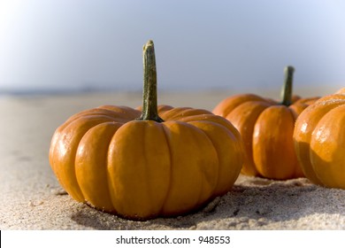 A couple mini pumpkins sitting on the sand at the beach.