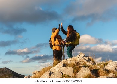 Couple of mountaineering hikers, with backpack and trekking poles, high-fiving as they reach the top of a mountain. Outdoor sports and weekend activities. - Shutterstock ID 2254520353
