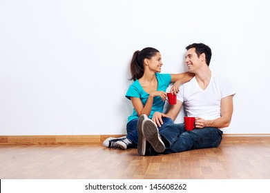 couple moving into empty new home sitting on floor together and drinking coffee - Powered by Shutterstock