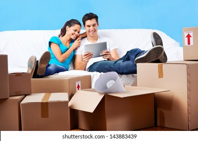 Couple Moving In Together Relaxing On Sofa Couch With Laptop Tablet Computer And Boxes