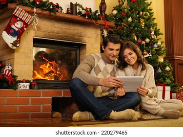 Couple near fireplace in Christmas decorated house with tablet pc