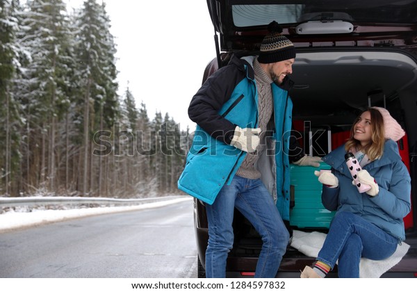 Couple near open car trunk full of luggage on\
road, space for text. Winter\
vacation