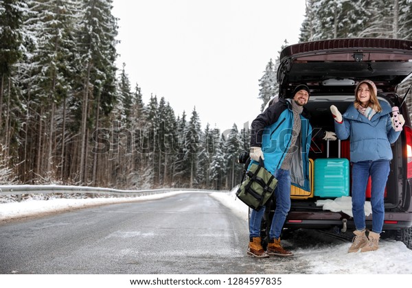 Couple near open car trunk full of luggage on\
road, space for text. Winter\
vacation