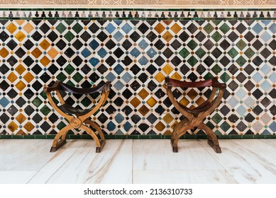 A couple of old wooden and leather chairs in front of a tiled wall in arabesque and Muslim colors. Antique armchair from the alhambra of granada. Rest concept