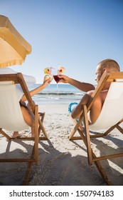 Couple on the beach clinking their glasses while relaxing on their deck chairs