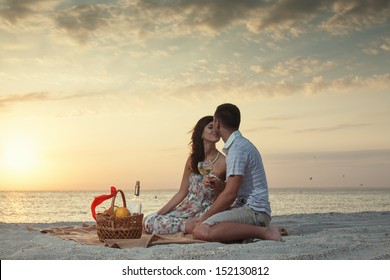 Couple On Beach With Luxury Wine Picnic during beautiful sunset. Dawn