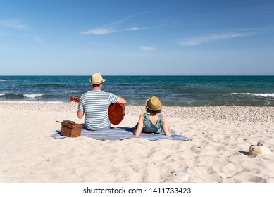 Couple On Beach, Man Playing A Spanish Guitar And Woman Laying Down. Mediterranean Vibes