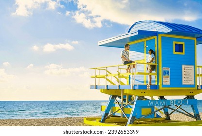 a couple on the beach in Miami Florida, a lifeguard hut in Miami beach, Asian women, and caucasian men on the beach during sunset. man and woman relaxing at a lifeguard hut looking at the ocean - Powered by Shutterstock