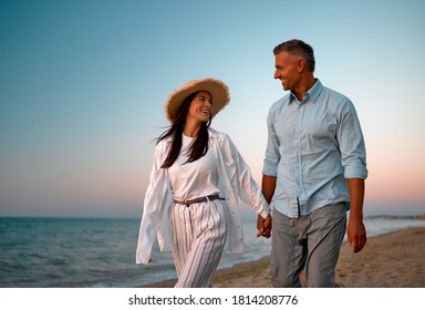 Couple on the beach. Traveling together to the sea. Handsome man and beautiful woman walking on the seashore and holding hands