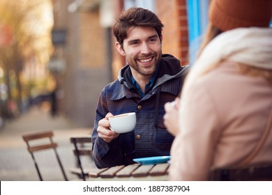 Couple On Date Sitting Outside Coffee Shop On Busy City High Street Looking At Digital Devices