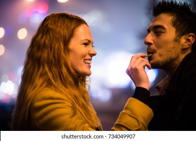 Couple On Date - Woman Feeds Her Boyfriend With Chocolate In Street At Winter Night