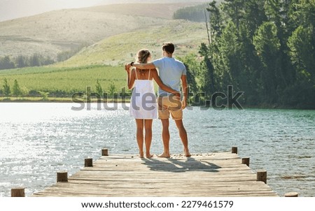 Couple on jetty by the lake, travel and relax together with nature and hug outdoor, love with care and bonding. Summer, holiday with man and woman back view, sunshine and relationship with trust
