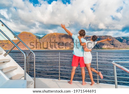 Couple on luxury yacht cruise ship tour at sunset feeling free happy with open arms in fun looking at mountain scenery. Romantic sunset boat ride watching view from deck on travel vacation.