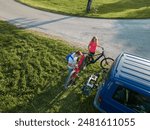 Couple on a nature recreational adventure, taking down electric mountain bikes from the bike rack on a van, aerial directly above shot.