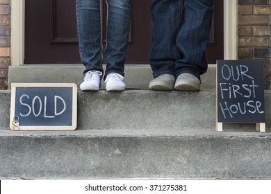 Couple On New Home Doorstep With Sold Sign And First House Sign