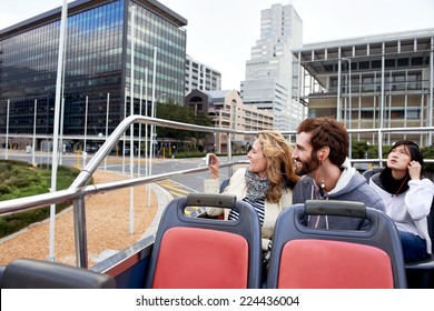 couple on open top tourist bus in city taking photos on vacation