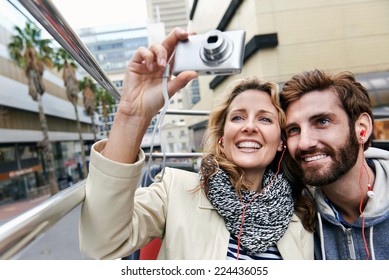 couple on open top tourist bus in city taking photos on vacation