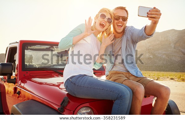 Couple\
On Road Trip Sit On Convertible Car Taking\
Selfie