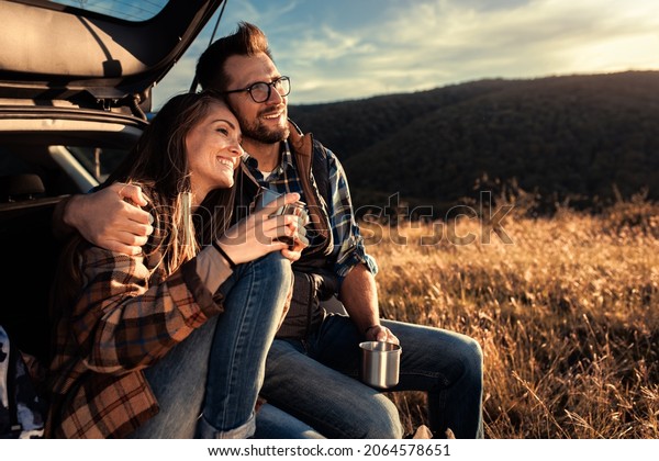 Couple on road trip sitting in trunk of a car
resting and drinking
coffee.