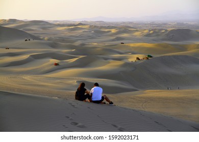 A couple on the sand dunes is watching people who do sand boarding, in Huacachina, Peru.  - Powered by Shutterstock