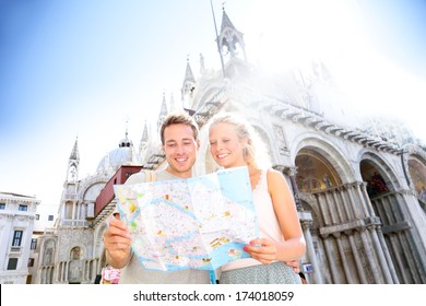 Couple On Travel Reading Map On In Venice, Italy On Piazza San Marco In Front Of Saint Mark's Basilica. Happy Young Couple On Travel Vacation In Europe. Happy Woman And Man In Love Traveling Together.