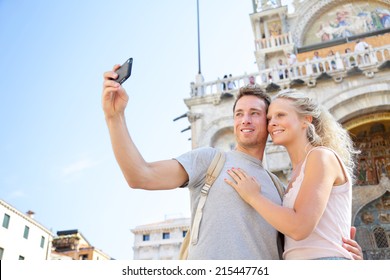 Couple On Travel Taking Selfie Photo Venice, Italy On Piazza San Marco In Front Of Saint Mark's Basilica. Happy Young Couple On Vacation In Europe. Happy Woman And Man In Love Traveling Together.