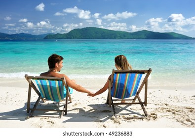 Couple On A Tropical Beach In Chaise Lounge