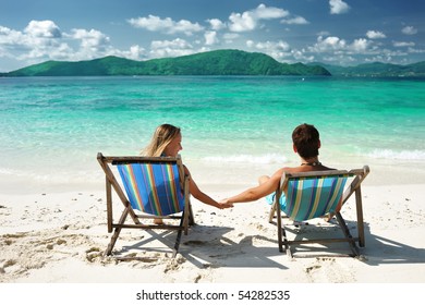 Couple On A Tropical Beach In Chaise Lounge