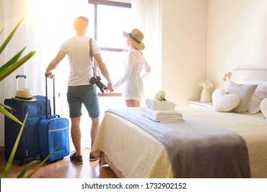 Verweilen Sie im Urlaub mit Koffern auf dem Rücken und schauen Sie aus einem Fenster in einem hellen Hotelzimmer.