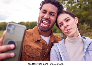 Couple On Walk In Countryside Pulling Funny Faces As They Take Selfie On Mobile Phone