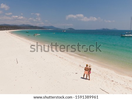 Couple on Whitsundays beach aerial view, with turquoise ocean, white sand. Dramatic DRONE view from above. Travel, holiday, vacation, paradise. Shot in Whitsundays Islands, Queenstown, Australia.