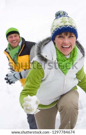 Couple on winter vacation having snowball fight together smiling at camera