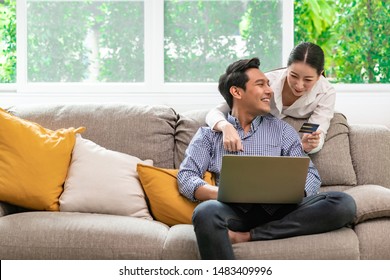 Couple Online Shopping At Home In Living Room Sofa. Asian Man And Woman, Man Looking At Woman.