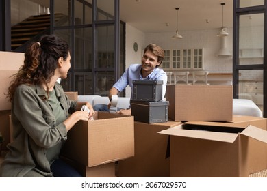 Couple pack their belongings preparing for moving to new own house, husband sealing box with adhesive tape, wife collects personal stuff, heap of cardboard boxes in living room. Concept of relocation - Shutterstock ID 2067029570