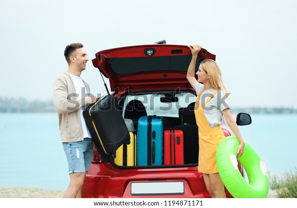 Couple\
packing suitcases in car trunk on\
riverside
