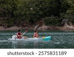 Couple paddling on lake or river in a canoe or kayak, outside in nature with trees and rocks in background; man and woman wearing life jackets in small canoe and travelling down a river
